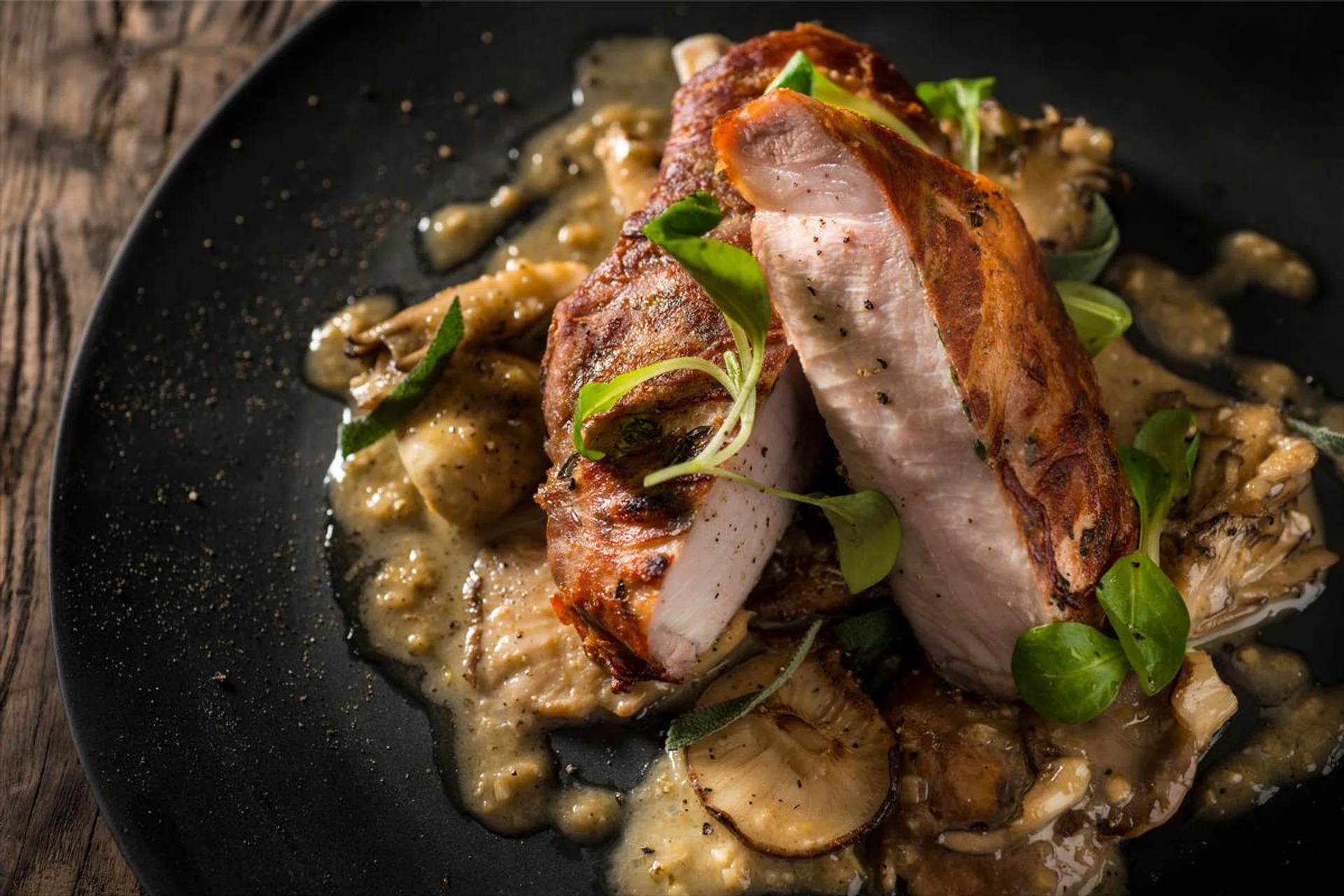 Prosciutto wapped Berkshire pork chop with mushrooms and sage in a white wine sauce on a pewter plate on a rustic wood background prepared by Jean-Georges Vongerichten, chef/owner of The Inn at Pound Ridge, NY.