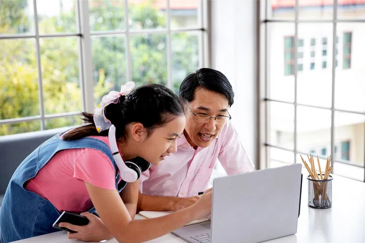 Asian family Father teaches daughter books by using laptop computer lying on the floor in the living room. Happy asian studying at home, study online