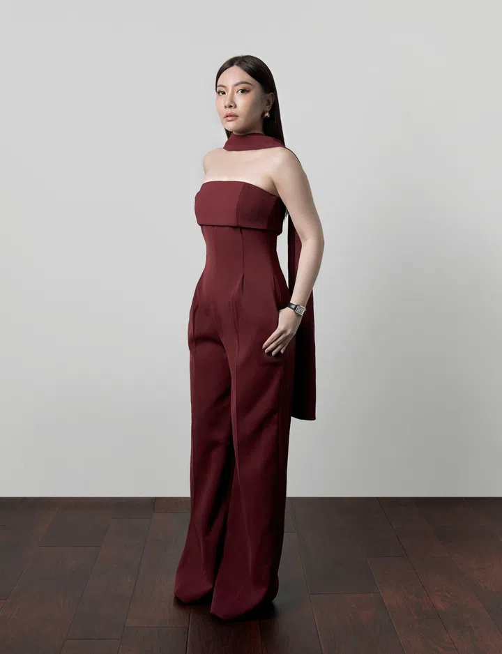 Ang Jinyuan身穿 Chello ICON x Ang Jin Yuan 酒红色无肩带连身裤装，站在浅灰色背景前，神情坚定，自信优雅。The Millennial Talk Ang Jinyuan, Style Lease和The Ivory Bridal创办人。礼服和婚纱租赁品牌。