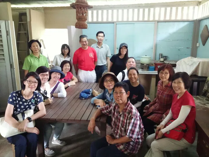 参与者在甘榜Lorong Buangkok的导览中合影留念，大家围坐在木桌旁，聆听讲解员分享新加坡最后一个甘榜的生活故事与珍贵回忆。哪里可以用SG Culture Pass？文化通行证活动推荐