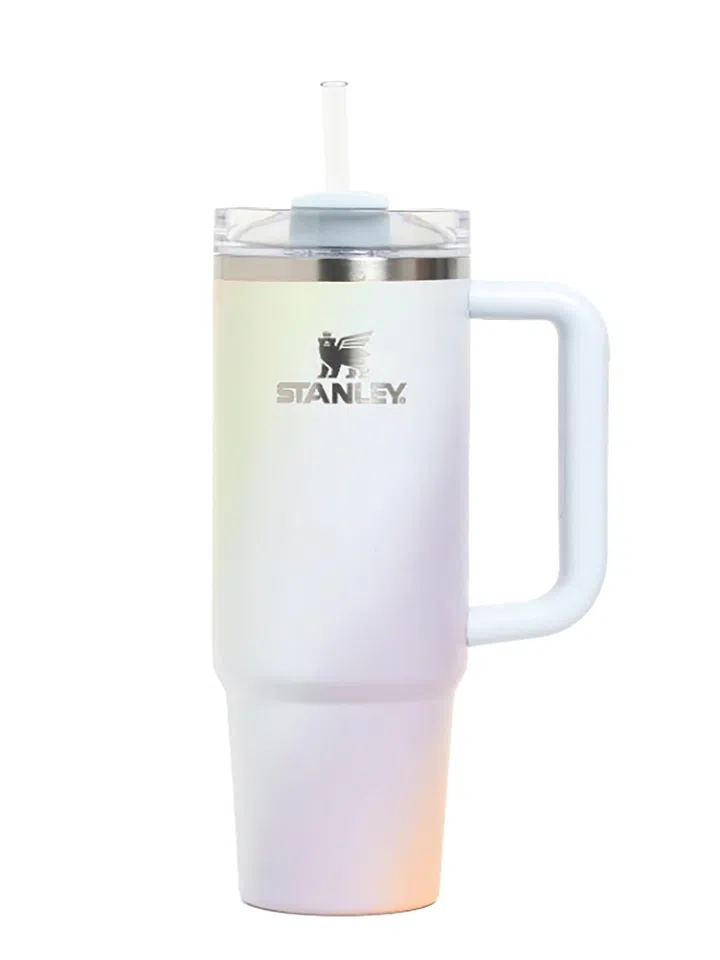Stanley虹彩随行杯，浅色杯身呈现淡黄、浅蓝、粉紫与浅橙交织的珠光效果，正面饰有银色品牌名称与标志。右侧配浅蓝色大握柄，顶部为透明杯盖、浅蓝色盖片及透明直吸管，杯口带银色金属饰边。