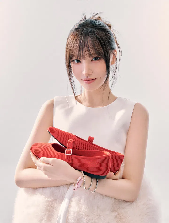 图片展示韩国女团IVE成员Liz手持一双红色VIVAIA Margot Mary-Jane平底鞋的时尚形象照。Liz身穿简约的浅色无袖上衣，搭配自然清新的妆发造型，面带微笑直视镜头，整体气质优雅温柔。她双手抱着一双亮眼的红色Mary Jane鞋款，鞋面为针织质感材质，搭配方头设计与可调节扣带，呈现简洁而时髦的外观。画面背景为干净明亮的浅色调，突显鞋款的鲜艳色彩与精致细节，整体氛围轻盈时尚，适合作为新年穿搭的舒适鞋款选择；2026新年鞋推荐：舒适好穿又好看的拜年鞋款。