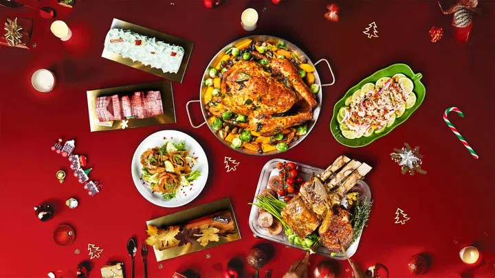 红色背景上的一桌 21 on Rajah “Shiokalicious” 圣诞飨宴，包括新加坡“叉烧”风味慢烤全火鸡、星式黑胡椒蜂蜜烧烤酱战斧牛排、仁当威灵顿牛肉、辣番茄烤火鸡、柠檬奶油咸蛋虾、节日沙拉、节日甜点如圣诞树桐蛋糕和水果蛋糕等。整体呈现融合本地风味与东南亚辛香料的丰富圣诞佳肴。圣诞大餐吃什么？新加坡9家必订自助餐全攻略