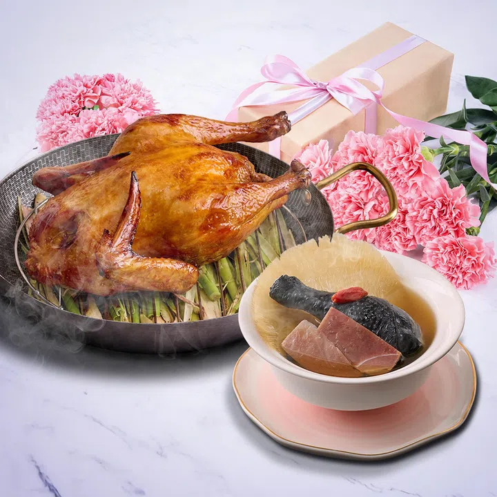 Jia He Grand母亲节套餐料理图：画面摆放香气十足的烧鸡与滋补炖汤，搭配粉色康乃馨与礼盒点缀，整体充满温馨节庆氛围。烧鸡外皮金黄油亮，炖汤内可见花胶与乌鸡等食材，展现精致又适合家庭团圆聚餐的粤式料理风格。2026母亲节餐厅精选指南