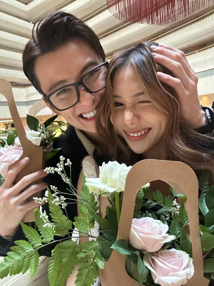 Edwin Goh与Rachel Wan在室内空间里亲密合影，两人开心贴脸微笑，Rachel捧着粉色与白色玫瑰花束，Edwin戴着黑框眼镜并轻抚她的头，画面洋溢甜蜜自然的幸福氛围。Rachel Wan：最好的感情，是让我更像自己