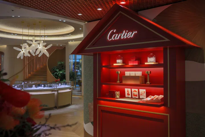 Cartier Festive Atelier 圣诞装置于新加坡精品店内呈现，红色主题空间陈列节日礼盒、丝带装饰与金色工具细节，展现品牌冬日故事灵感的沉浸式圣诞市集氛围。