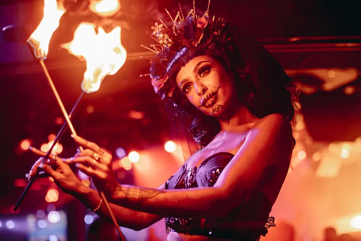 一名表演者身着黑色服饰与花冠，在火舞表演中展现万圣节派对氛围，背景灯光昏红。新加坡万圣节去哪里玩推荐。