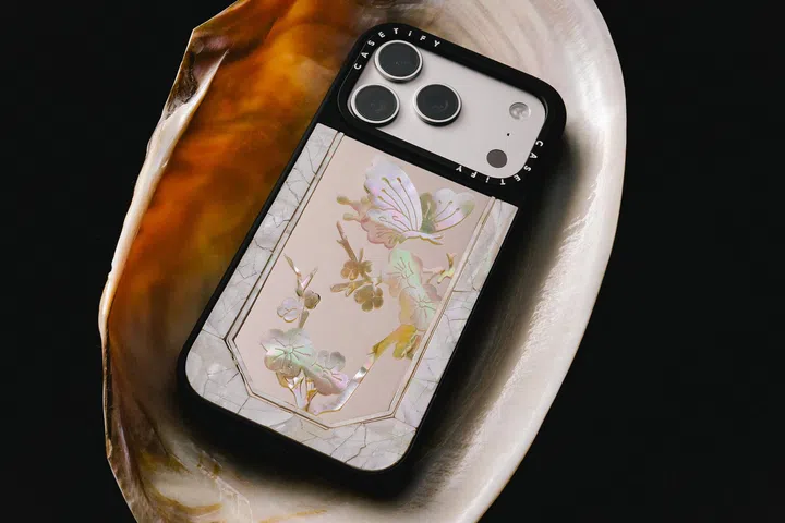 CASETiFY与Miss Sohee联名珍珠母贝手机壳，放置于贝壳上展示，手机壳以蝴蝶与花卉图案为设计主轴，呈现虹彩光泽与细腻纹理，搭配大理石质感边框与镜头保护设计，整体散发高定艺术感与优雅气质，展现时尚与科技配件的融合。