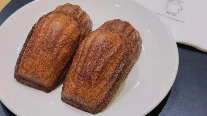 两块韩国脆皮牛油年糕（Butter tteok）摆放在白色餐盘上，表面呈现金棕色烘烤色泽与自然焦纹，外层酥脆、内部软糯Q弹；近距离拍摄突出其外酥内软的口感层次，背景为简约用餐环境，展现近期爆红的K-food甜点风格与质感。