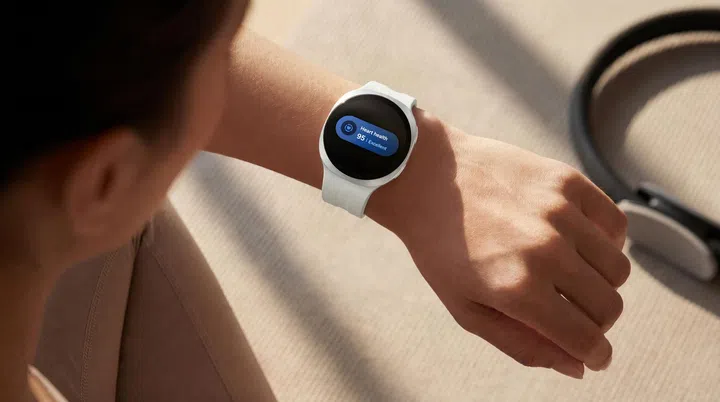 一名用户佩戴白色表带的Samsung Galaxy Watch9，低头查看手腕上的健康数据。Galaxy Watch9采用银色圆形表壳，屏幕显示Samsung Health的心脏健康（Heart Health）功能，健康评分为95分，并标示为“Excellent”。画面背景为阳光洒落的室内运动空间，旁边放置瑜伽垫及运动器材，营造健康生活氛围。整体画面展现Galaxy Watch9可随时查看健康数据、追踪身体状况，并协助用户养成日常健康管理习惯。