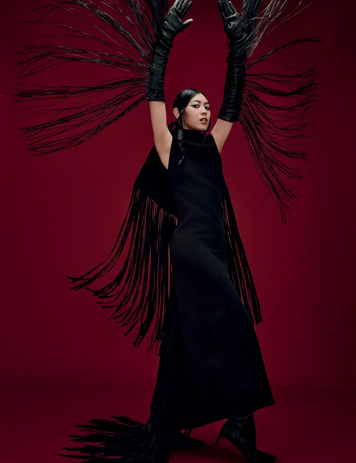 Jasmine Sokko身穿Sportmax无袖黑色连身裙，搭配长手套与高跟靴。她双手举起，裙子的流苏如翅膀般展开。