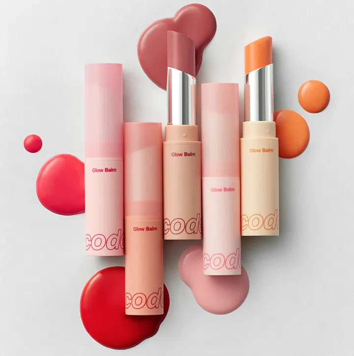 $20以下也能送出好礼：同事交换圣诞礼物精选。图中为 CODE GLOKOLOR Glow Lip Balm 多款色号，采用粉嫩渐层包装与不同色调的润唇膏展示，呈现适合作为日常美容小礼物的精致视觉。