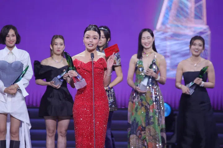 《红星大奖2026》现场，张颖双（Hazelle Teo）身穿红色礼服手持奖座在台上发表感言，同时举起红包分享得奖心情，身后多位艺人同台见证，气氛热烈动人。《红星大奖2026》首次入围“十大”的张颖双