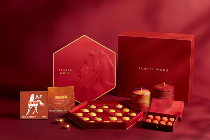 Janice Wong农历新年系列甜点礼盒陈列图。画面以喜庆红色为主调，展示多款马年限定巧克力与节庆礼盒，包括骏马造型设计包装盒、巧克力凤梨塔、柑橘造型巧克力以及多款精致小礼盒。整体摆设充满艺术感与节日氛围，适合作为新年送礼或拜年伴手礼的创意选择。2026马年新年送礼推荐：拜年礼盒与新年礼物精选