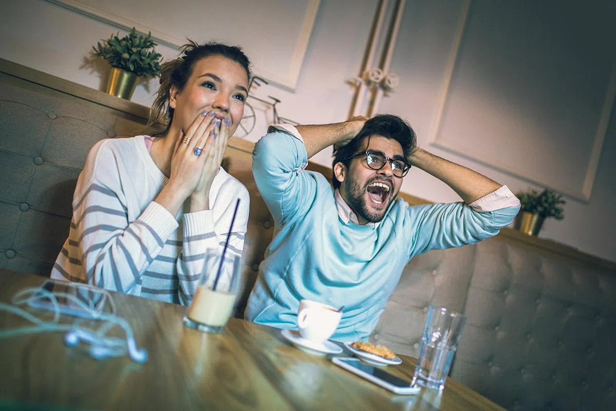 Modern couple in cafe looking excited and happy after their favorite football team scored a touchdown.