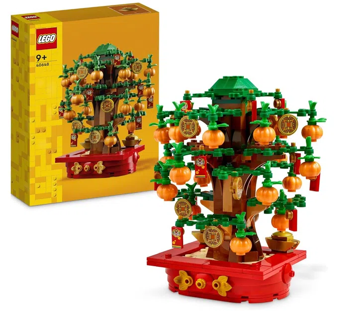 画面展示 LEGO Money Tree 摇钱树（40648）积木套装的完成模型与产品包装盒。主体为一棵积木拼搭的摇钱树，树干以棕色积木构成，枝叶为多层绿色积木结构，整体呈立体层次感。树枝上悬挂多颗橘色橘子造型装饰、金色钱币吊饰与红色红包挂件，营造浓厚的新春节庆氛围。底座为红色圆形平台，并点缀金色花纹装饰，增强喜庆视觉效果。左侧可见黄色外包装盒，上方印有产品图片与 LEGO 标志。整体配色以红、绿、橘与金色为主，呈现传统农历新年象征丰收、财富与祝福的意象，适合作为居家空间的新春摆设与亲子拼搭收藏。