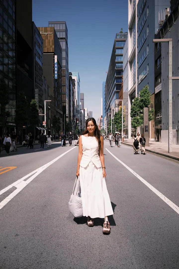 符芳榕穿着白色套装，站在东京街头的行人道中央，都市建筑林立。符芳榕，命运使者，离开演艺圈，专访