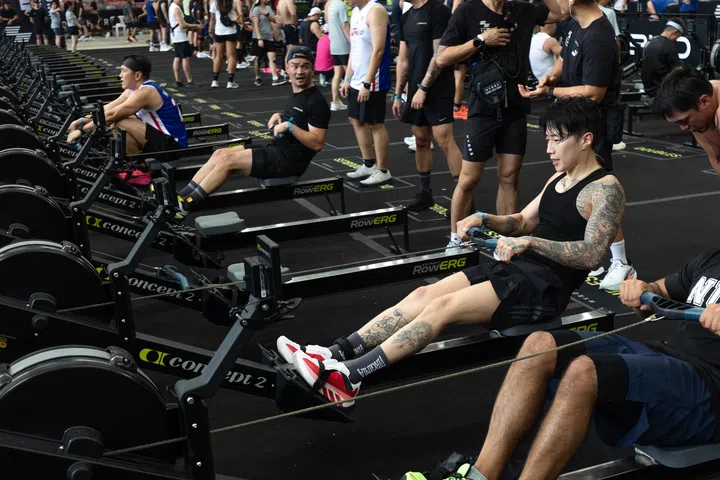 Jay Park在HYROX比赛中进行RowErg划船项目训练，专注完成拉动动作，腿部与手臂肌肉发力明显，现场多名参赛者同时进行比赛，气氛紧张而热烈。