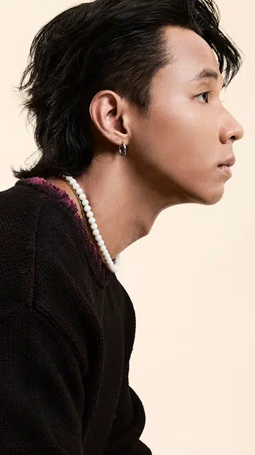 侧拍画面中，一位短发男子身穿深色针织上衣与白色珠串项链，侧身凝视前方，背景为柔和米色。画面右侧为灰色区块，上方以粉红文字写着“MEN WE LOVE 2025 × EDY LEE”，下方有《女友》NUYOU 的标志。此图为人物专访封面图，呈现他沉稳专注的神情与风格。