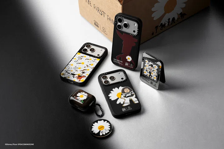 CASETiFY x Toy Story x PEACEMINUSONE联名科技配件宣传照，画面以黑灰渐层背景呈现多款手机壳及随身配件。手机壳设计结合《Toy Story》角色与PEACEMINUSONE标志性的白色Daisy雏菊图案，包括以满版雏菊搭配Woody元素的款式、以Buzz Lightyear搭配大型雏菊的黑色手机壳，以及另一款以深色角色剪影配上小雏菊的设计。画面中还展示耳机保护壳、圆形配件及折叠支架，均延续黑、白、黄为主的视觉风格。后方棕色包装盒印有“THE FIRST FAN”字样及Toy Story、PEACEMINUSONE相关图案，整体呈现鲜明的街头感与收藏感。