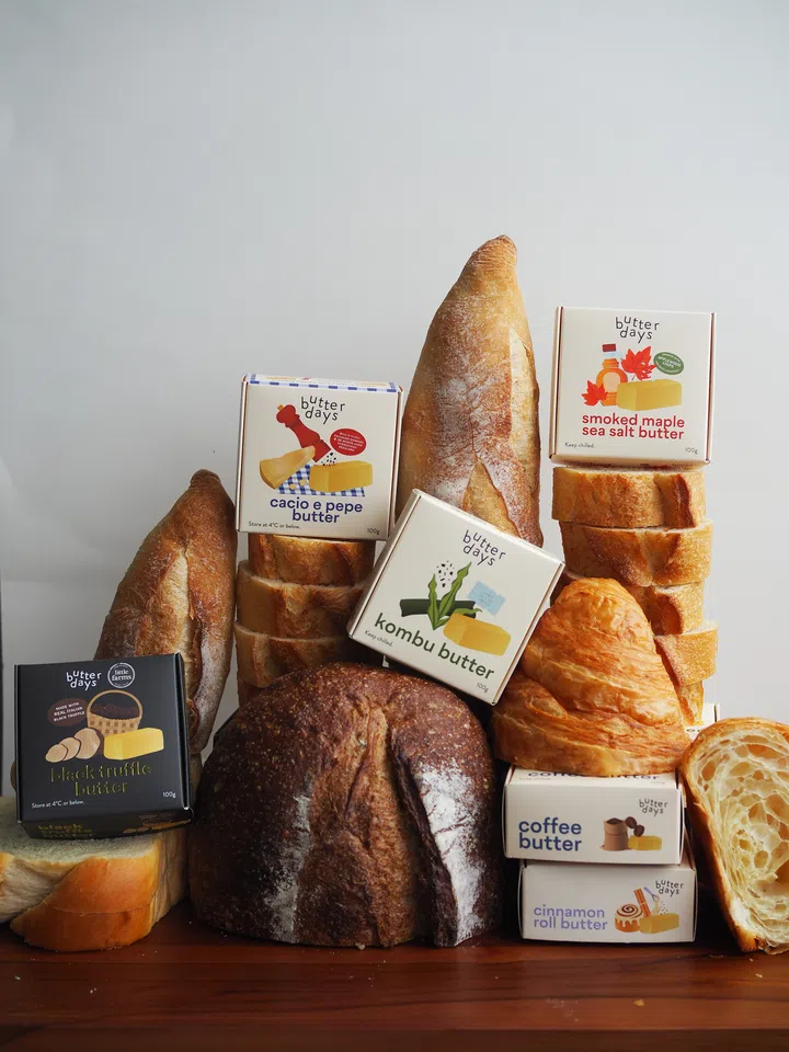 $20以下也能送出好礼：同事交换圣诞礼物精选。图中陈列 Butter Days 多款调味奶油，包括昆布、黑松露、咖啡、肉桂卷等口味，搭配法棍、吐司与可颂，呈现美食礼物的丰富选择。