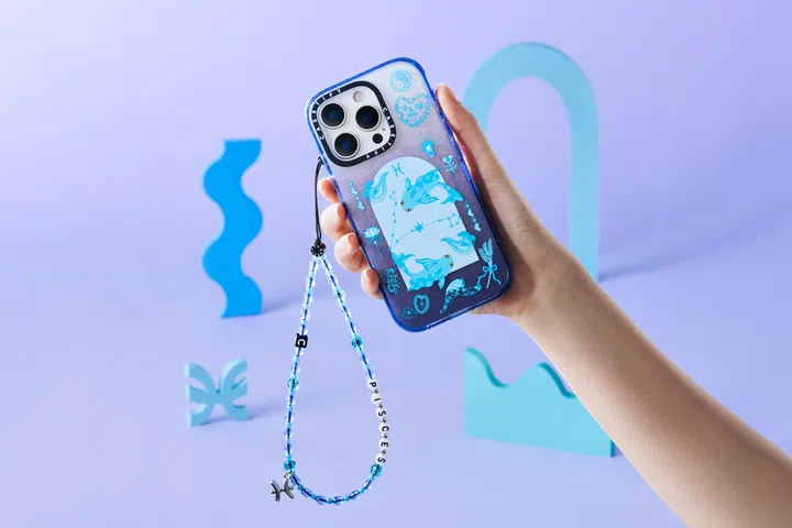 一只手举起蓝紫色渐变的手机壳，上面有双鱼座插画与星座符号，挂着蓝色与白色串珠挂绳，背景为紫色与蓝色几何装饰，整体呈现梦幻星座风格。CASETiFY星座系列中的双鱼座设计。高颜值手机壳推荐。
