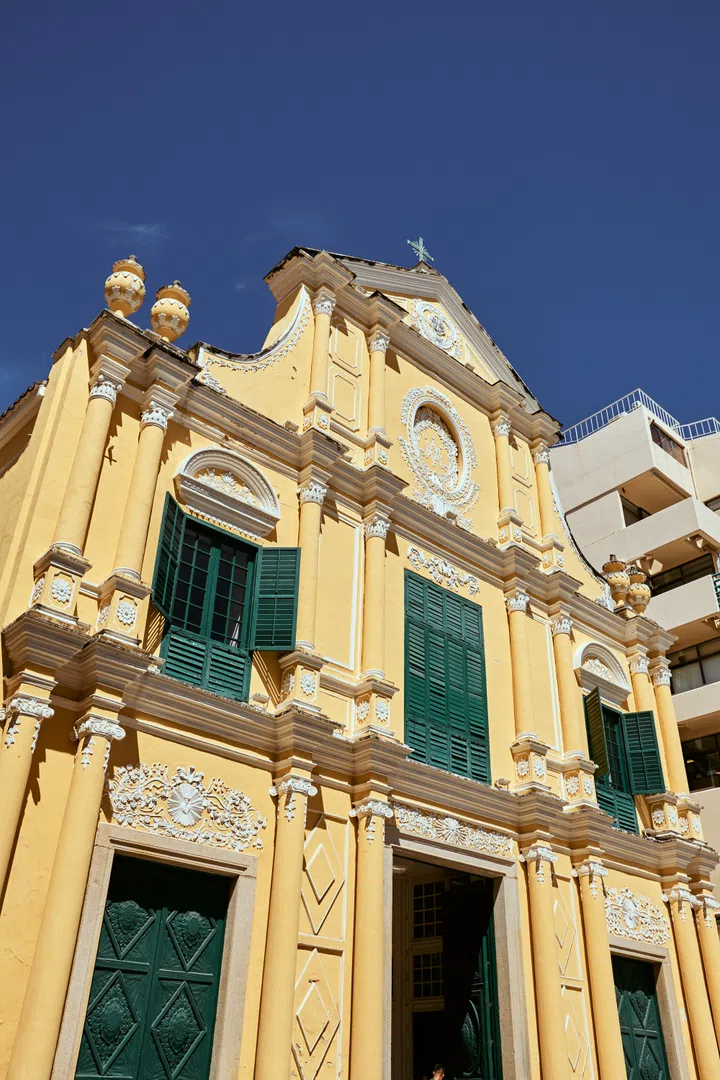 澳门玫瑰堂（St. Dominic’s Church）外观，黄色立面与绿色百叶窗在阳光下格外明亮，融合葡式与南欧建筑风格，是澳门历史城区的著名地标与热门打卡景点。澳门3天2夜旅游攻略。