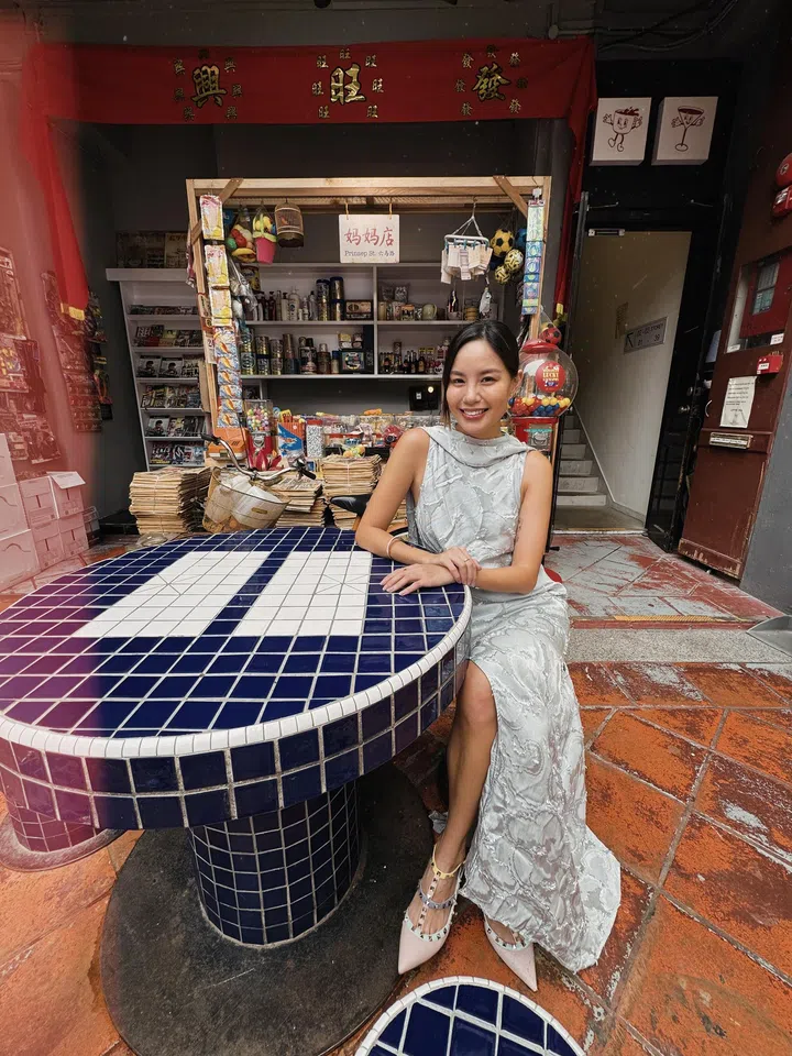 符芳榕身穿银灰色长裙，坐在复古蓝白瓷砖桌旁，背景是怀旧杂货铺。符芳榕，命运使者，离开演艺圈，专访
