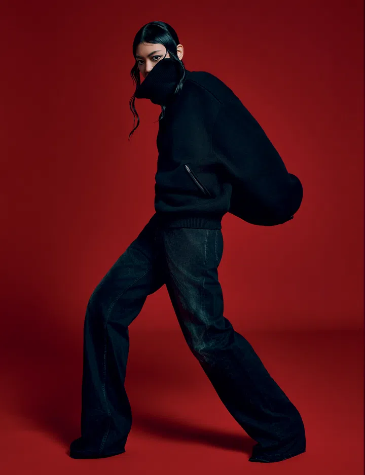 Jasmine Sokko身穿黑色Balenciaga套头衫与深蓝色宽松长裤，背景为红色，她摆出强烈有力的姿态，整体造型前卫、张力十足。