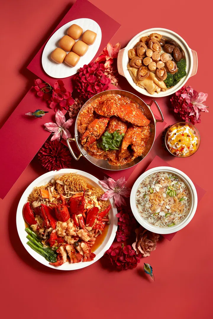 农历新年外带年菜摆盘展示图，红色背景上摆放多道中式佳肴，包括一锅招牌辣椒蟹、鲍鱼与香菇配西兰花的滋补砂锅菜、龙虾配生面、一道热汤羹类料理，以及一盘金黄小馒头与甜品，周围点缀红色花卉装饰，整体呈现丰盛热闹的团圆饭氛围，适合新加坡农历新年外卖与家庭聚餐场景。