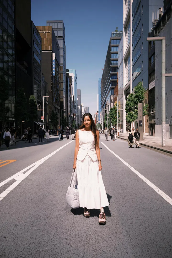 符芳榕穿着白色套装，站在东京街头的行人道中央，都市建筑林立。符芳榕，命运使者，离开演艺圈，专访