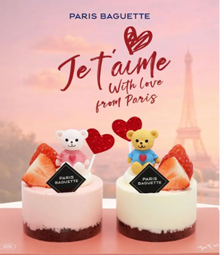 Paris Baguette 情人节限定 Sweetheart Couple Bear Short Cake Set 展示于粉色背景前，整体画面营造出甜美浪漫的节日氛围。画面中央摆放两款迷你圆形蛋糕，分别为粉色与白色蛋糕体，底部为深色蛋糕层，上方装饰新鲜草莓切片与品牌标志牌。每款蛋糕上方各有一只可爱小熊装饰，一只为白色小熊穿粉色上衣，另一只为黄色小熊穿蓝色上衣，两者胸前均点缀爱心图案，并搭配红色爱心装饰，象征情侣之间的甜蜜与陪伴。背景印有“PARIS BAGUETTE”与“Je t’aime With Love from Paris”字样，并可见巴黎铁塔轮廓，呼应法式情人节主题。整体视觉呈现精致、可爱且充满节日气氛，突显迷你蛋糕作为情人节甜点礼物的分享感与仪式感。2026情人节礼物推荐：10款精致礼物让TA一秒心动