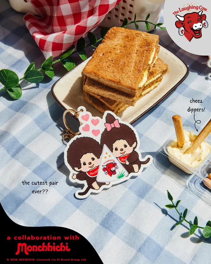 The Laughing Cow x Monchhichi联名宣传图，以蓝白格纹野餐布为背景，中央展示一款限定Monchhichi钥匙扣。钥匙扣上是一对Monchhichi角色，其中一只戴着粉色蝴蝶结，两只角色围在The Laughing Cow经典三角芝士包装旁，周围点缀粉色爱心。后方餐盘上摆着烤至金黄的吐司，右侧则有Cheez Dippers芝士蘸酱与面包棒。画面右上角印有The Laughing Cow品牌标志，左下角则写有与Monchhichi合作的字样，整体以野餐场景突出联名的可爱、轻松与收藏感。