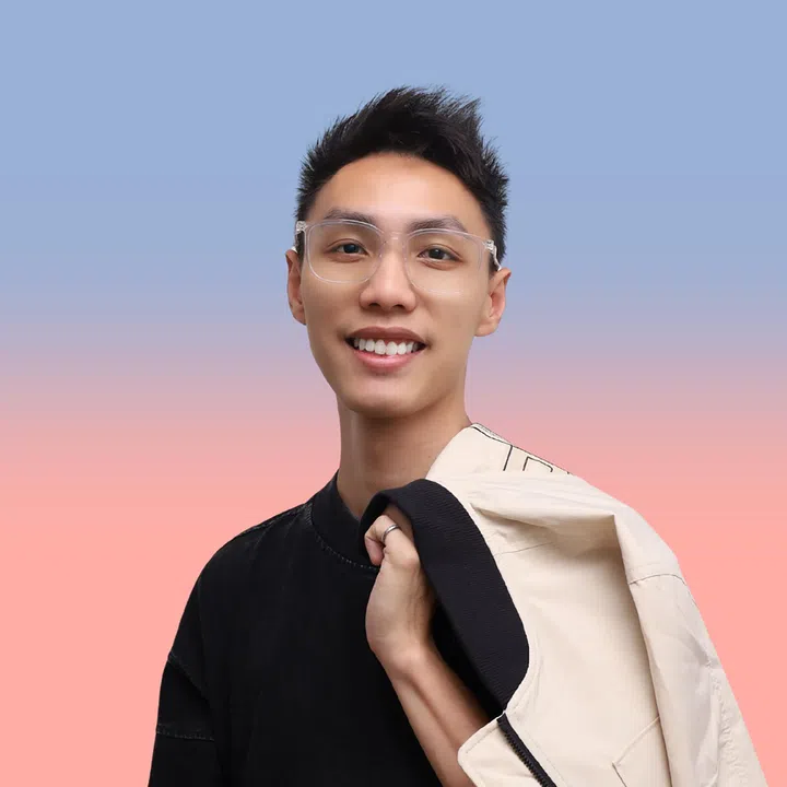 新加坡导演 Jason Lee 的半身肖像照，他短发、戴透明框眼镜，微笑看向镜头，身穿黑色上衣，浅色外套随意搭在肩上，背景为蓝粉渐层色调，呈现轻松而自信的形象，配合其首次执导院线长片《百万红包》的专访内容。