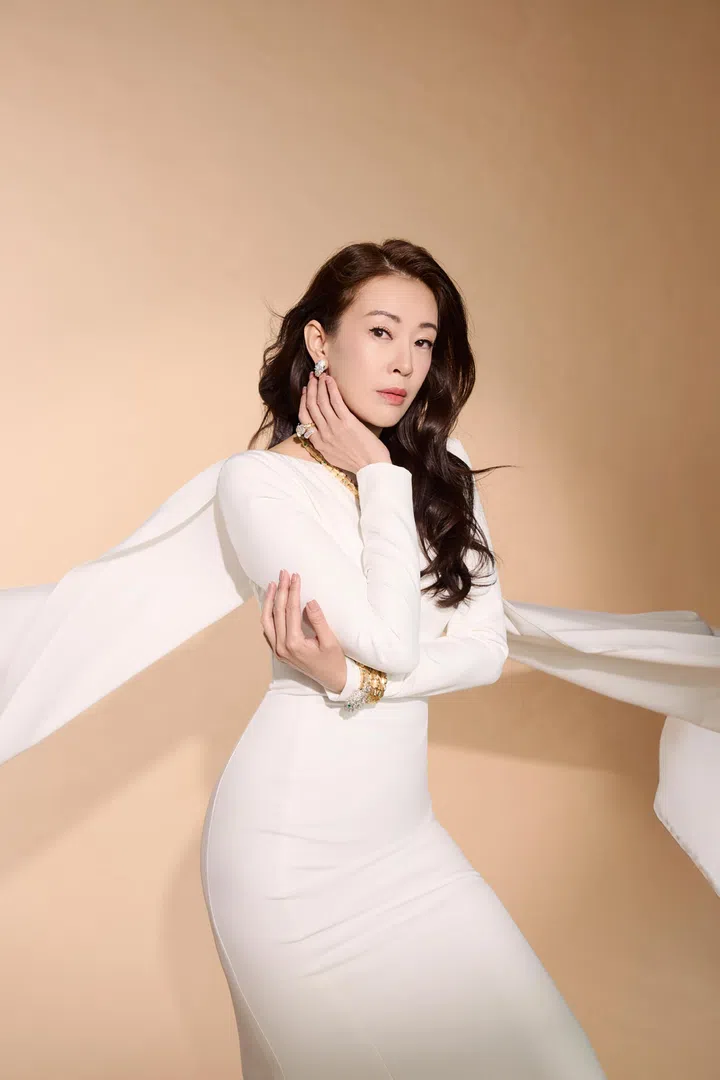 这是一张棚内拍摄的人物时尚肖像照。刘子绚身穿一袭贴身剪裁的白色长礼服，整体线条流畅，勾勒出优雅身形。礼服袖部延伸出轻盈飘逸的披肩布料，在身后自然展开，营造出动态与层次感，让画面更具时尚张力。
她微微侧身站立，一手轻触脸颊，另一手环抱手臂，姿态柔美而自信。长发自然披肩，带有轻微波浪弧度，妆容精致干净，眼神平静而坚定，直视镜头，展现成熟从容的气质。配饰方面，她佩戴了简约却亮眼的珠宝，包括耳环、戒指与手链，为整体造型增添细节与质感。
背景为温暖的米色渐变色调，光线柔和均匀，没有复杂元素干扰，使人物成为画面唯一焦点。整体氛围简洁高级，突显刘子绚优雅、沉稳且具有力量感的女性形象。刘子绚首夺视后：22年7次提名终圆梦，她把时间走成答案