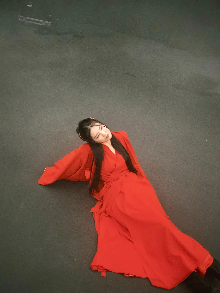 Ferlyn饰演《带剑女孩》中的化成风，身穿红色长袍坐在深色地面上，长发垂落，画面构图简洁而富有戏剧感。