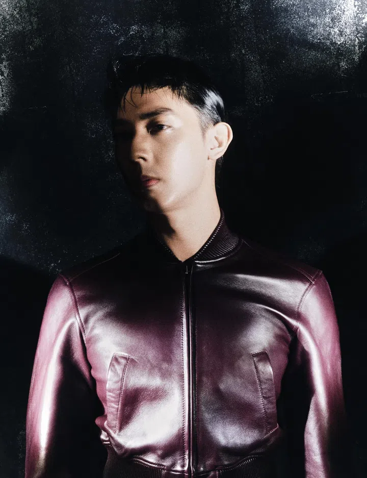 仲伟杰时尚人像，身穿光泽感皮革外套，站于深色背景前，光影突出面部轮廓与服装质感，整体风格沉稳且富有力量感。