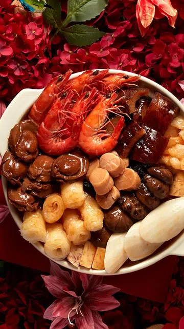 并排展示的两款新春盆菜，左侧白色砂锅盛装多种海味与配料，包括整只红虾、鲍鱼、花菇、鱼鳔、白萝卜与豆制品，摆放在红色花卉背景上；右侧陶瓷盆菜以鲍鱼、干贝、整虾、鱼肉与菌菇为主，食材层层铺排，背景为浅色桌布与餐具，呈现新加坡农历新年团圆饭常见的盆菜摆设。