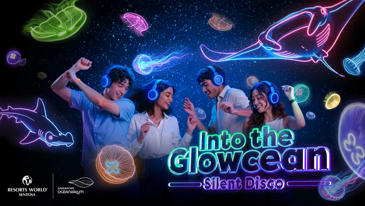 Resorts World Sentosa 旗下 Singapore Oceanarium 的 Into the Glowcean Silent Disco 横版活动宣传图。四名年轻男女戴着蓝色发光无线耳机，在深蓝色的海洋主题背景前随着音乐舞动。周围环绕紫色、绿色、粉红色及蓝色霓虹灯勾勒的水母、魔鬼鱼和鲨鱼图案，右下角展示“Into the Glowcean Silent Disco”字样，左下方印有 Resorts World Sentosa 与 Singapore Oceanarium 标志。