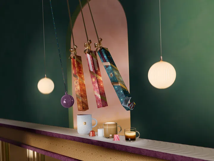 $20以下也能送出好礼：同事交换圣诞礼物精选。图中展示 Nespresso 节日限定咖啡胶囊与杯具，搭配缤纷的节日吊饰与暖色灯光，营造优雅且充满节庆感的礼物氛围。