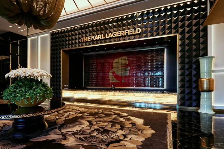 澳门THE KARL LAGERFELD酒店大堂内部，中央摆放鲜花装饰，背景墙上以红黑色块拼出卡尔·拉格斐侧脸剪影，整体设计以黑金色调为主，彰显奢华与时尚气息。