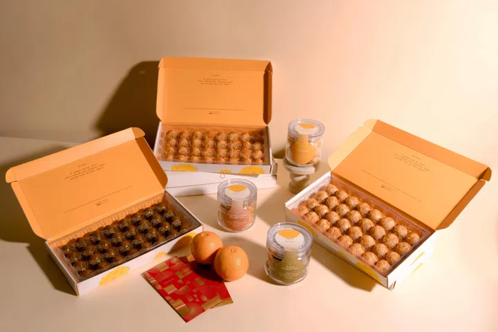 nesuto农历新年凤梨酥系列产品陈列图。画面中展示多盒打开的凤梨酥礼盒与玻璃罐装凤梨酥，包括经典黄油香草、焙茶与创意口味款式，金黄色点心整齐排列，搭配新年红包与柑橘点缀，整体以温暖柔和的节庆色调呈现，营造精致温馨的新年送礼氛围。2026马年新年送礼推荐：拜年礼盒与新年礼物精选