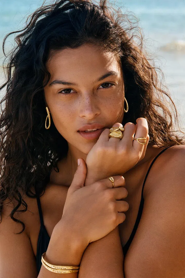 Model wearing stacked Pandora Essence rings, bangles and drop earrings with sculptural curves.