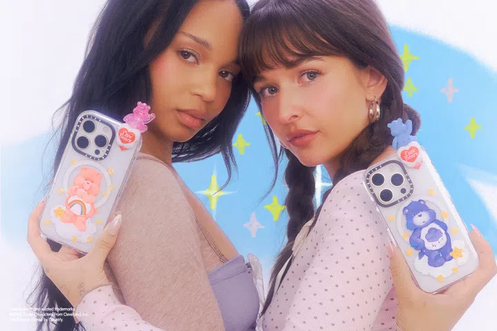 CASETiFY 与 Care Bears 联名系列形象照，两位模特手持透明手机壳，壳内点缀粉色与蓝色 Care Bears 立体装饰、彩虹与星星图案，并搭配同系列小熊造型挂饰，背景为梦幻蓝色星星元素，呈现可爱风格的限量联名手机壳与配件设计，适合喜爱角色联名与个性化手机配件的消费者。