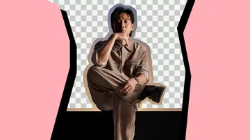 戚玉武身穿浅棕色服装坐姿沉稳，神情专注，在粉色与黑色图形背景前展现出成熟而内敛的气质，呼应他以导演身份推出短片《Cendol》的主题。