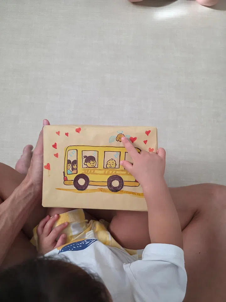 画面中，陈泂江的女儿坐在他腿上，手指着一张手绘黄巴士的画纸，巴士窗里画着一家人的笑脸与爱犬，背景布满红色爱心，象征温馨家庭与童趣创作。陈泂江独家专访。