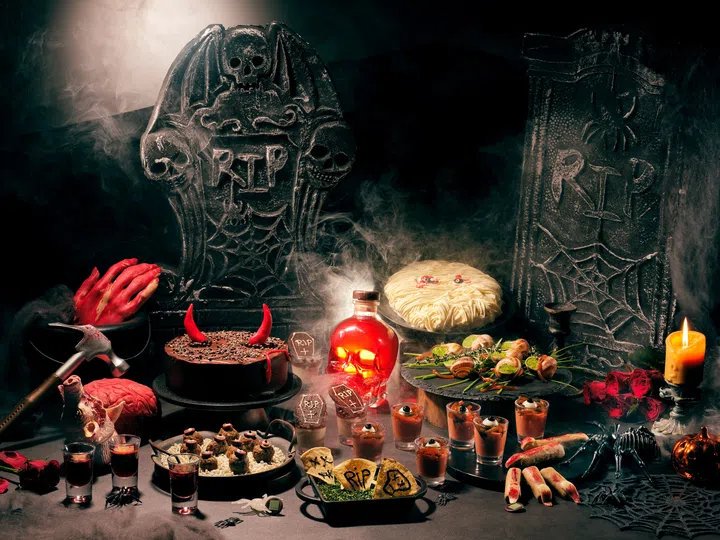 Lime Restaurant 2026万圣节限定 SubLIME Halloween 自助餐美食展示。深色餐桌上摆放恶魔角造型巧克力蛋糕、眼球造型甜点杯、墓碑饼干、以骷髅手指为灵感制作的点心，以及搭配香草与青酱的蜗牛料理。背景布置刻有骷髅及“RIP”字样的黑色墓碑，周围点缀红色骷髅酒瓶、仿真断手、蜘蛛、蜡烛与烟雾，营造诡异而充满创意的万圣节用餐氛围。