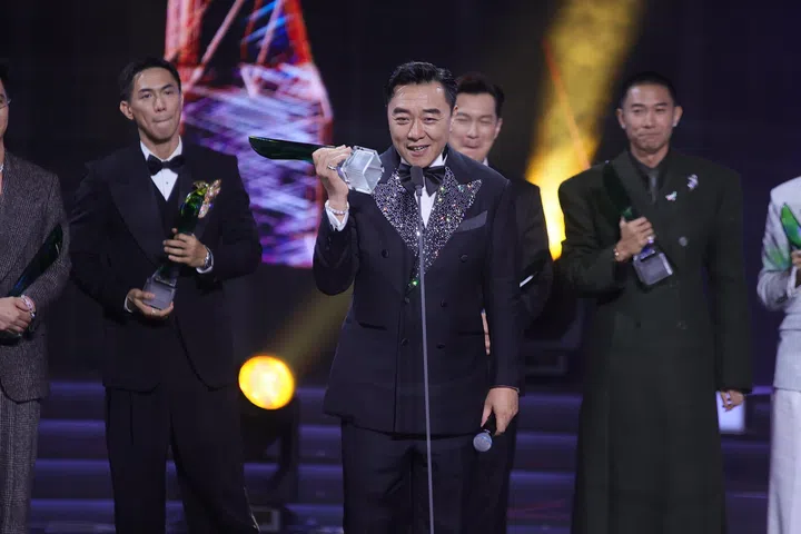 《红星大奖2026》现场，郭亮手持奖座在台上发表感言，身穿黑色礼服站在舞台中央，其他得奖艺人站在身后鼓掌致意，灯光聚焦下气氛热烈，见证他获奖的高光时刻。《红星大奖2026》从“听牌”晋升超级红星的郭亮