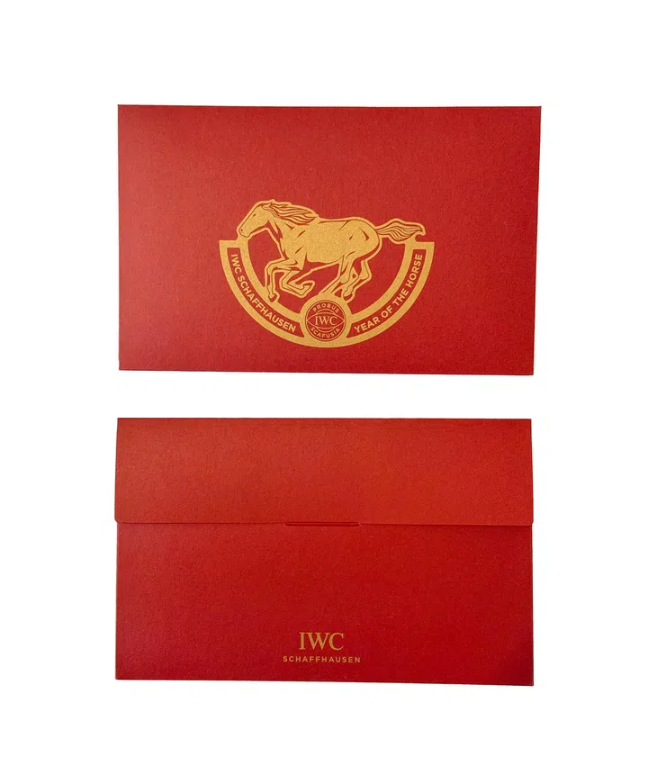 IWC Schaffhausen 2026马年红包封正反面设计展示，红包封整体采用质感细腻的红色底色，搭配中央金色压印图案。正面呈现一匹奔跑中的骏马，置于弧形徽章之上，徽章上印有“IWC SCHAFFHAUSEN”和“YEAR OF THE HORSE”字样，下方为品牌经典标志，象征力量、速度与马年的吉祥寓意。背面为简约信封式设计，下方印有“IWC SCHAFFHAUSEN”金色品牌字样，整体设计低调典雅，融合品牌制表传统与农历新年节庆元素，呈现精致且具有收藏价值的新年红包封。2026马年红包封盘点：今年的新年红包设计，你最喜欢哪一个？