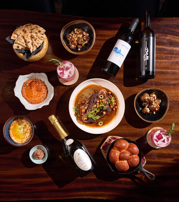 Fat Prince 的圣诞 Festive Christmas Bundle 摆在木桌上，包括中东香料焖牛肋排、烤面包、蘸酱、季节蔬菜、甜点及鸡尾酒，展现中东与地中海风格的节庆料理组合。2025圣诞外带套餐推荐：在家享用超值又美味的圣诞大餐